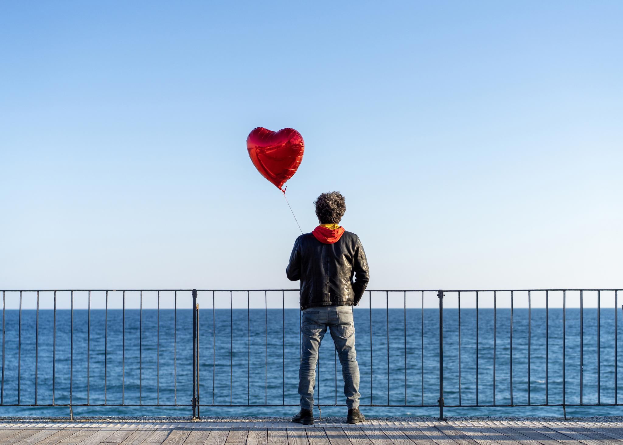 Einsamer Mann, der einen roten herzförmigen Ballon am Strand hält Männerherzen Männer dialoge 11-2025